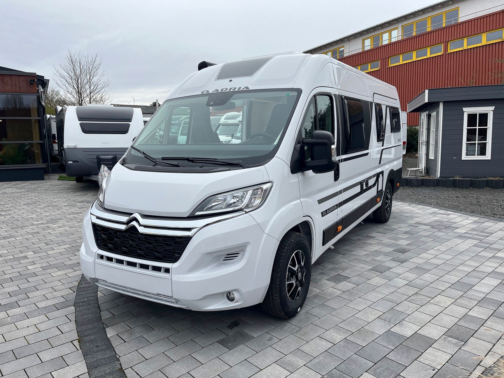 Frontansicht des Wohnmobils auf einem Parkplatz vor einem Gebäude.