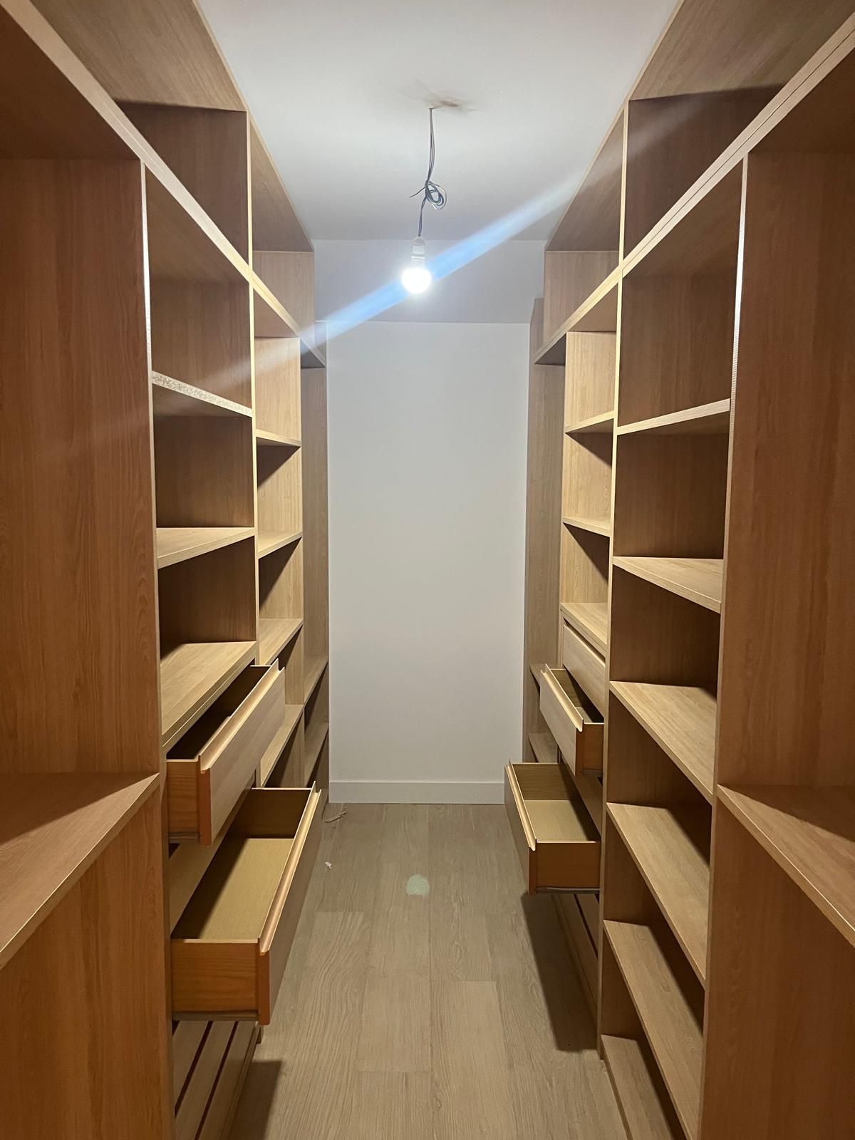 Vestidor con estanterías de madera en tonos claros y cajones a ambos lados del espacio.