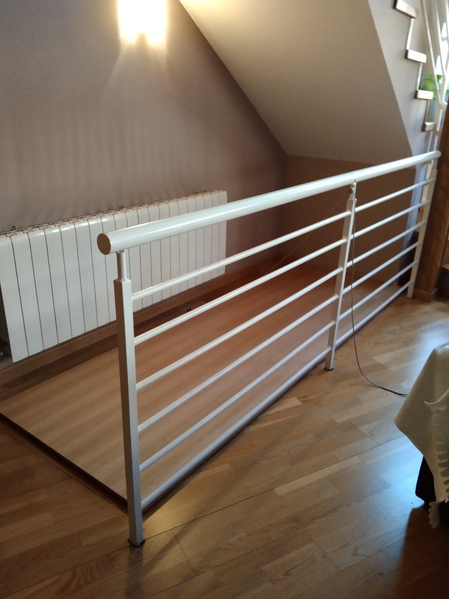 Una barandilla blanca sobre un suelo de madera, junto a una pared inclinada y un radiador.