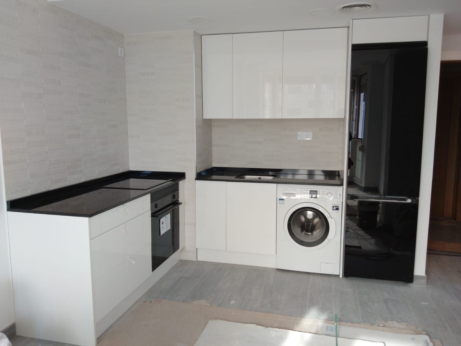 Cocina moderna blanca con encimeras y electrodomésticos negros. Incluye horno, estufa, lavadora y refrigerador.