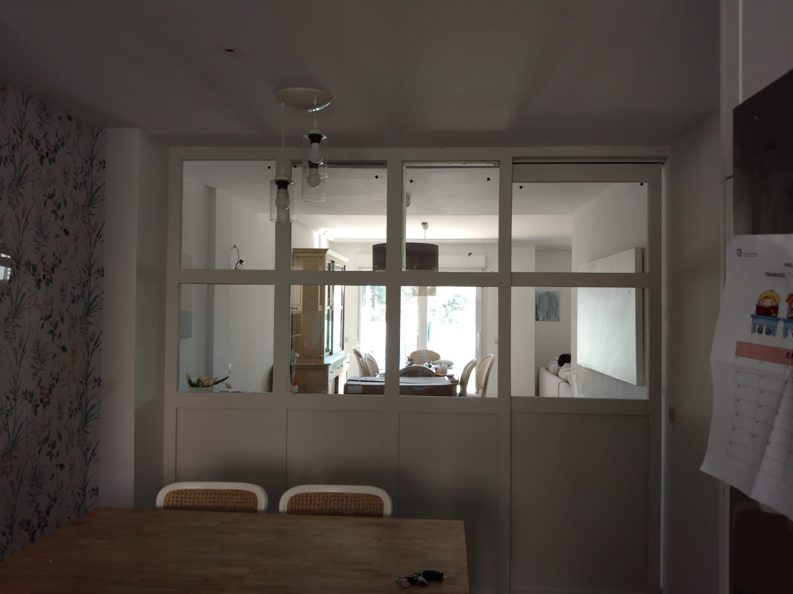 Vista interior de una habitación con una mampara de cristal con marco blanco. Vista hacia el comedor, con luz natural.