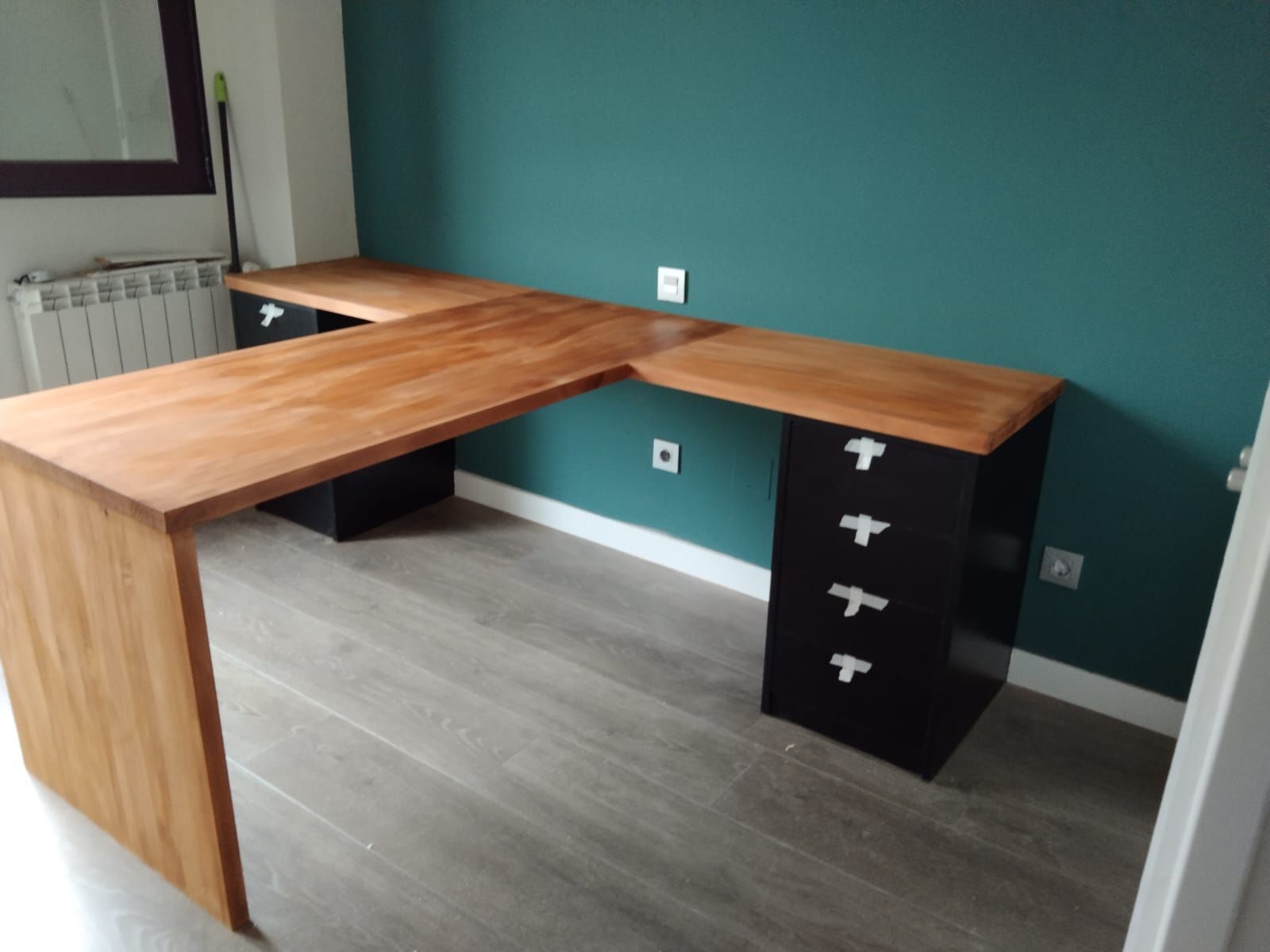 Escritorio de madera en forma de L con cajones, color negro con tiradores blancos, en una habitación con pared 