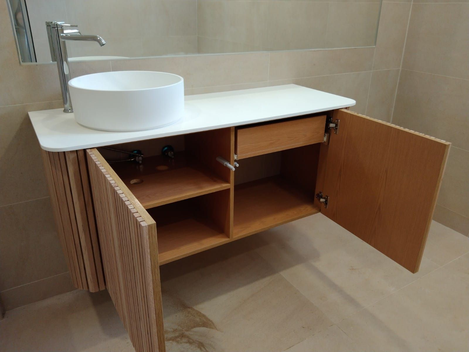 Mueble de baño con encimera blanca, lavabo blanco y mueble de madera con puertas abiertas.
