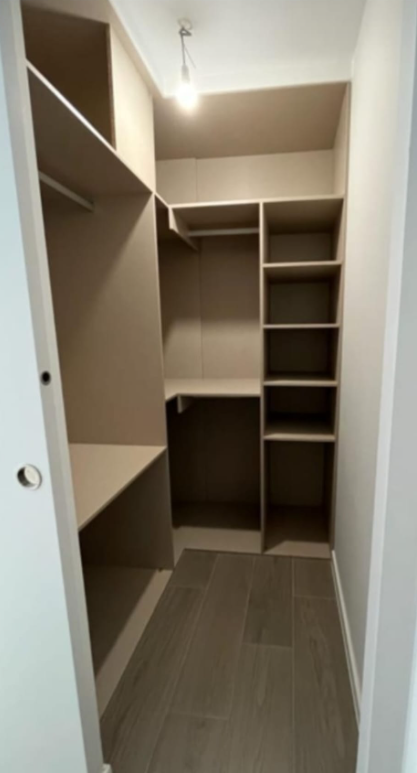 Armario empotrado con estantes y barras para colgar. Estanterías beige y suelo de madera clara.