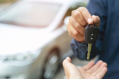 Handing over car keys to an open palm beside a blurred white car