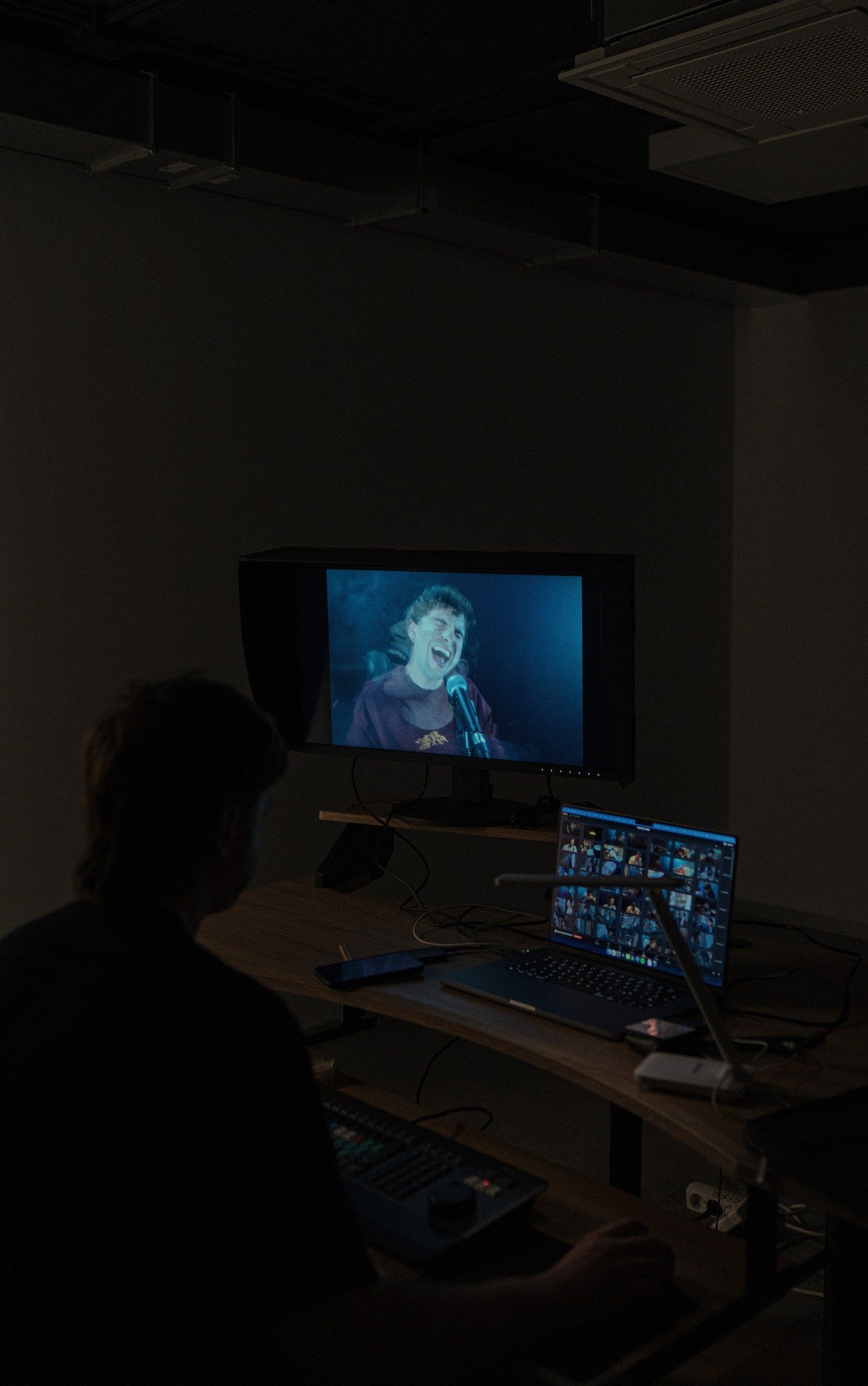 Un hombre está sentado frente a una pantalla de computadora en una habitación oscura.