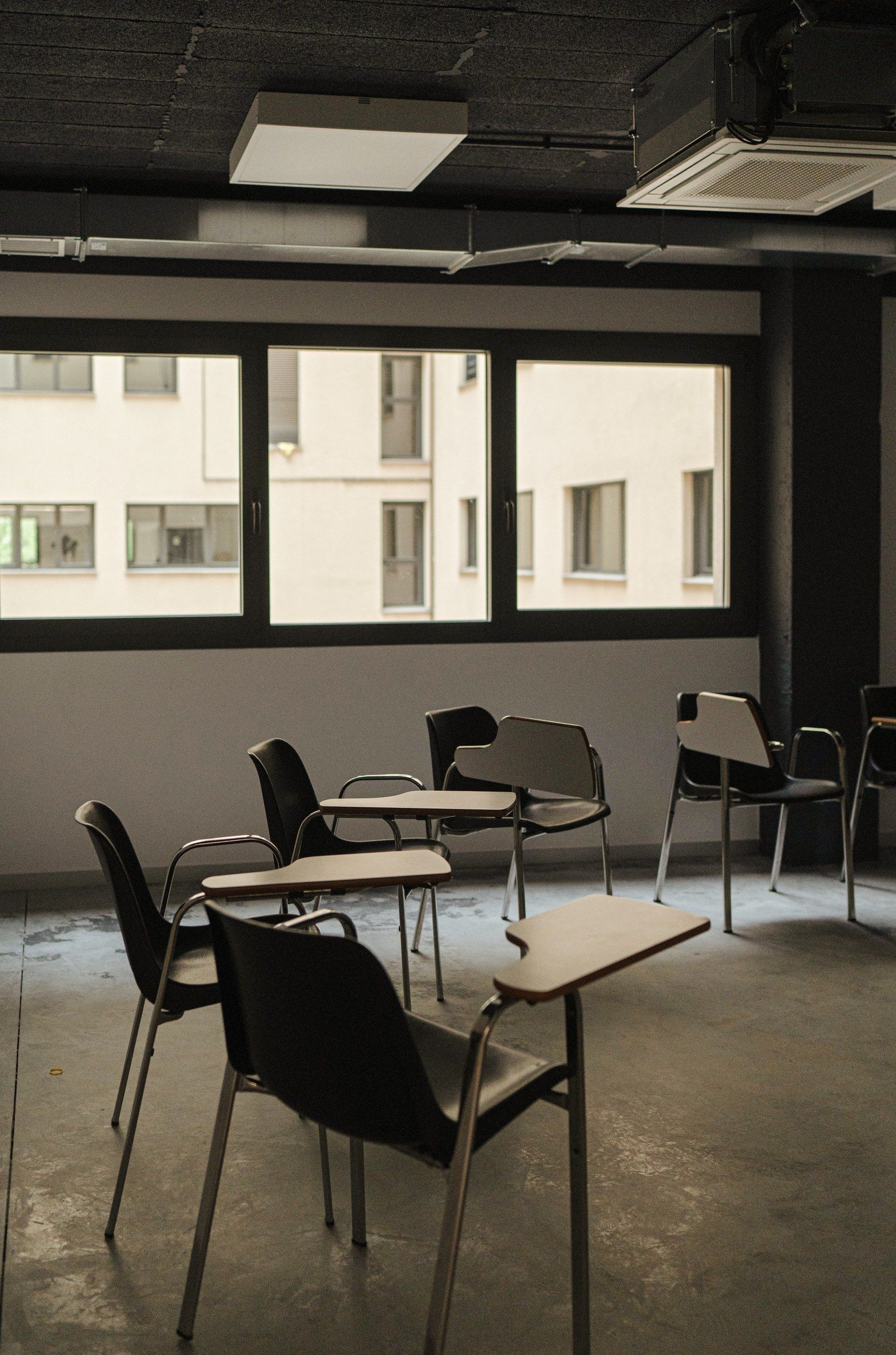 Una fotografía en blanco y negro de un aula con mesas y sillas.