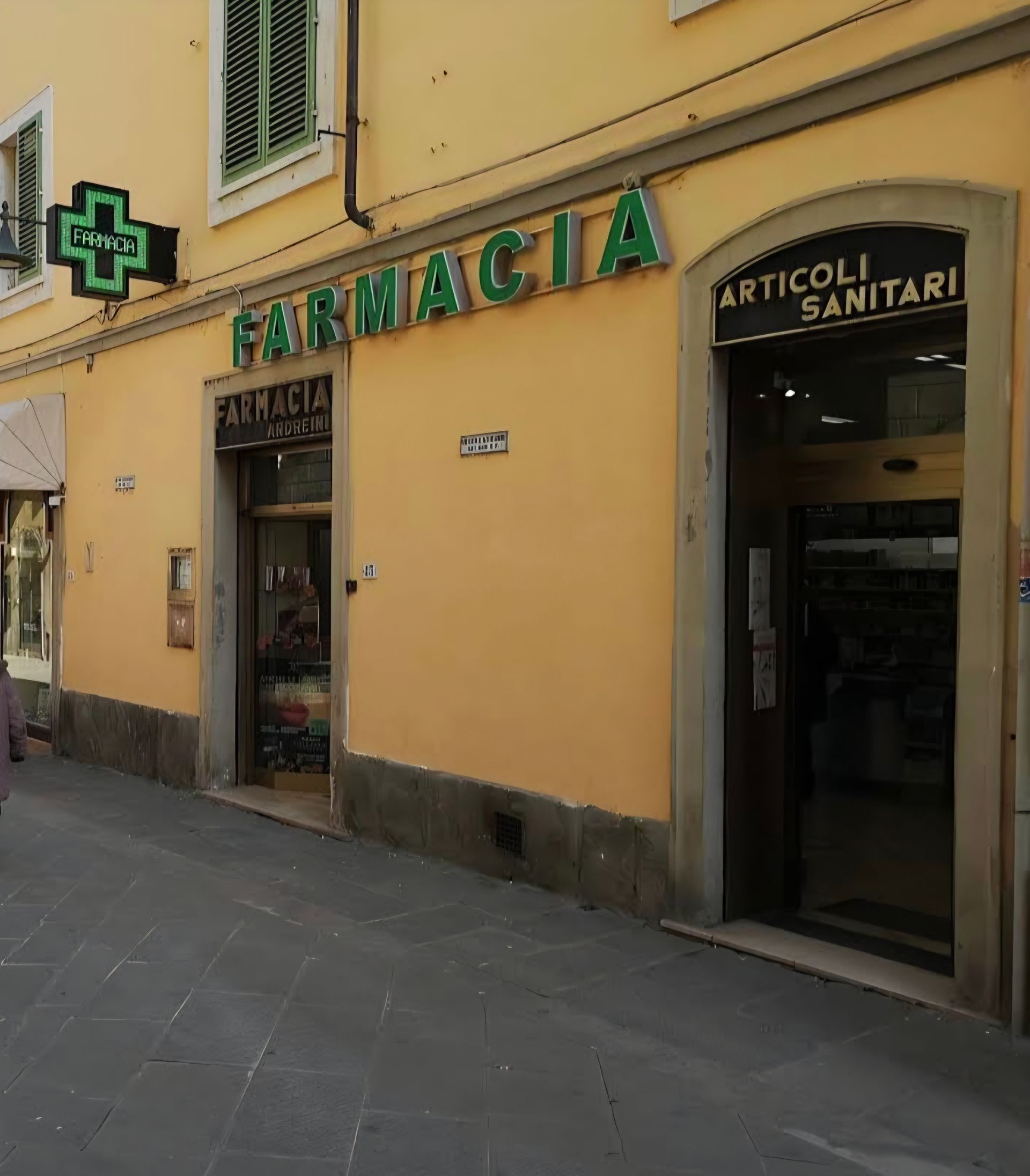 Vista interna di una farmacia con scaffali pieni di prodotti, un bancone e segnaletica sul pavimento per il distanziamento.