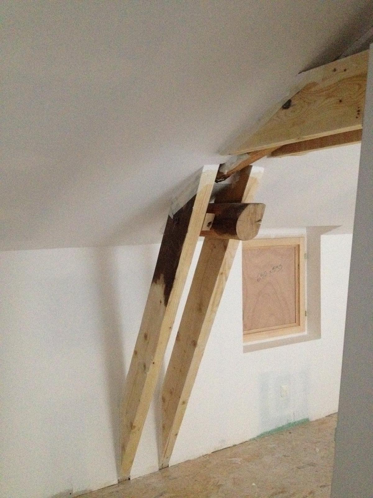 Structure de support en bois construite dans un grenier, avec une fenêtre visible dans le mur.