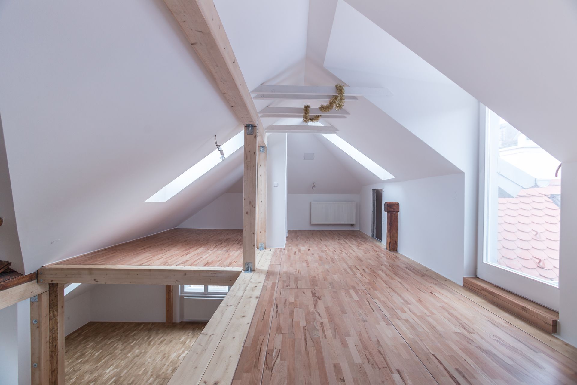 Intérieur de type loft avec parquet et poutres apparentes ; lumière naturelle provenant des puits de lumière et des fenêtres.