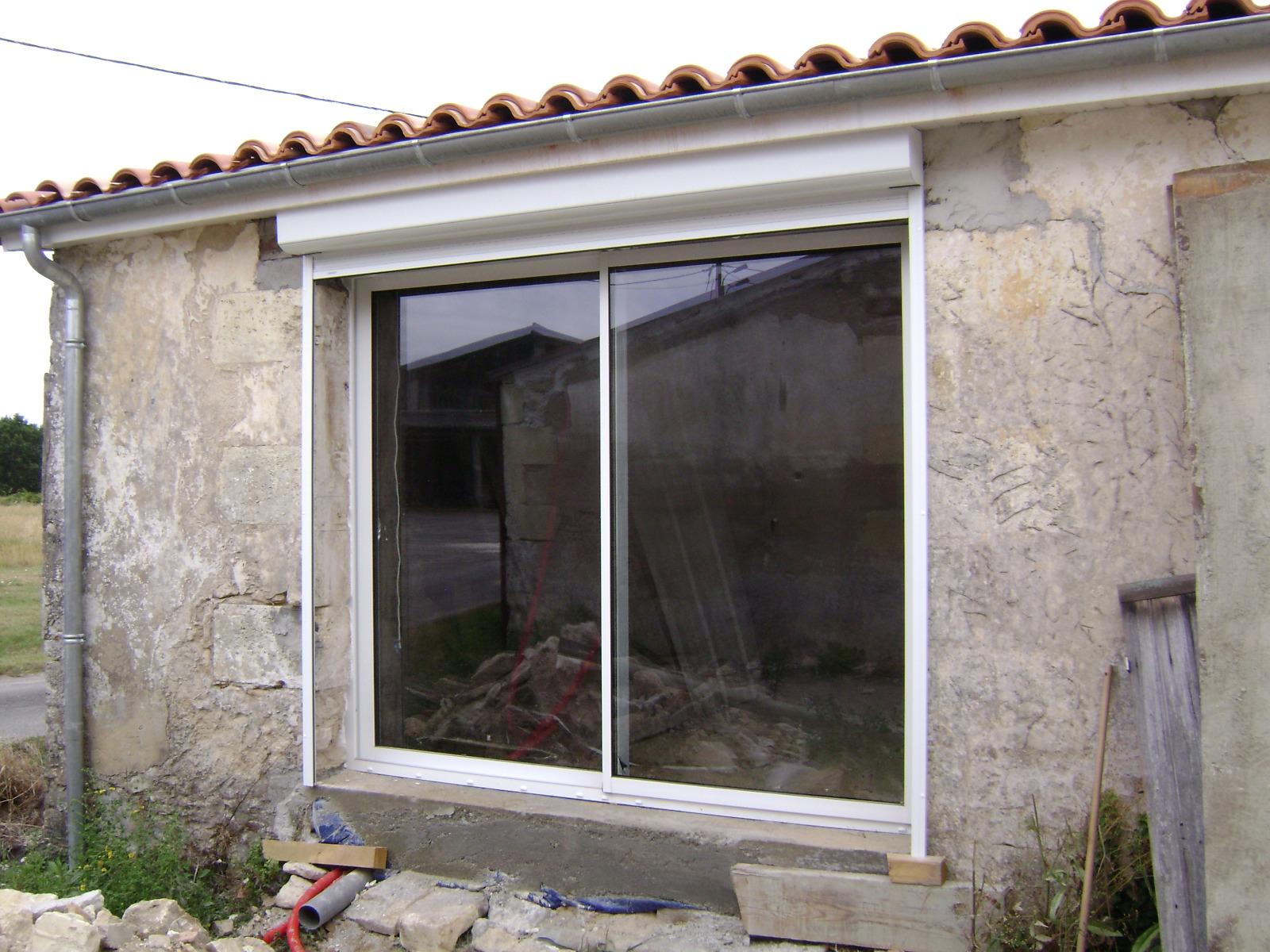 Fenêtre à cadre blanc et volet roulant sur un bâtiment délabré.
