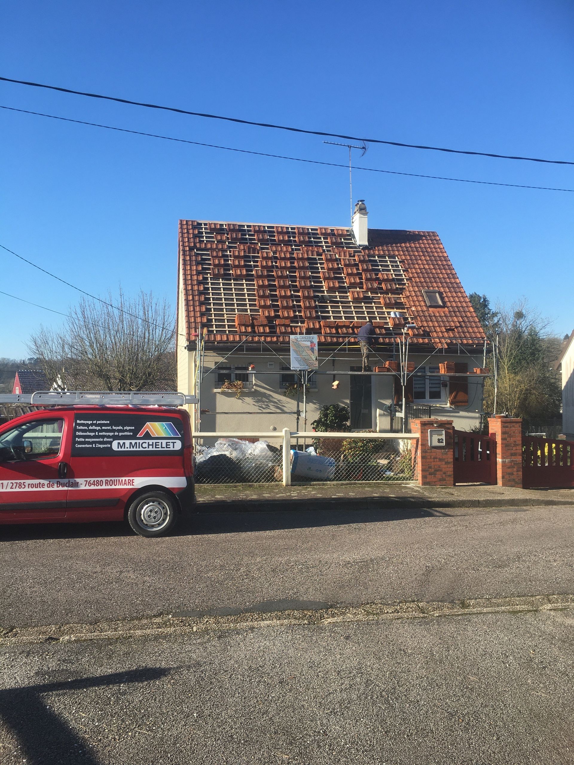 Une camionnette rouge garée près d'une maison endommagée, au toit partiellement effondré, par une journée ensoleillée.