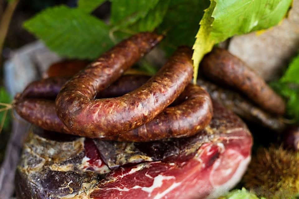 Dans un cadre rustique en plein air, une spirale de saucisse sombre et séchée repose sur une tranche de viande séchée et du feuillage.