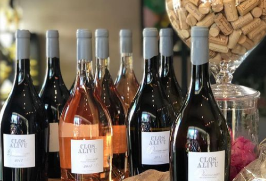 Une collection de bouteilles de vin Clos Alivu, comprenant des variétés rosées et rouges, est posée à côté d'un bol en verre rempli de bouchons de liège.
