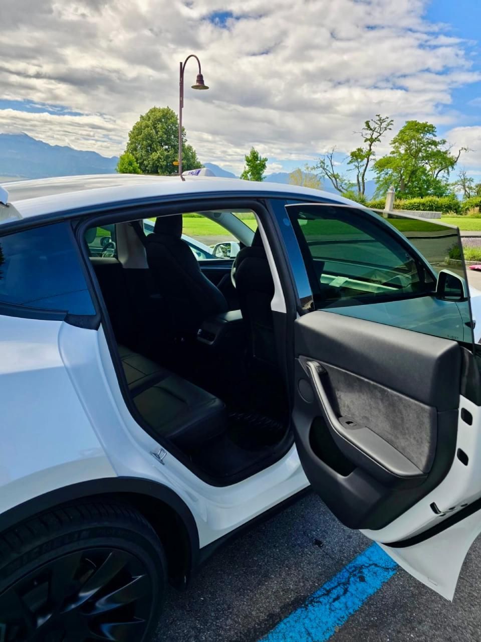 Une Tesla Model Y blanche est garée dans un parking avec ses portes ouvertes.