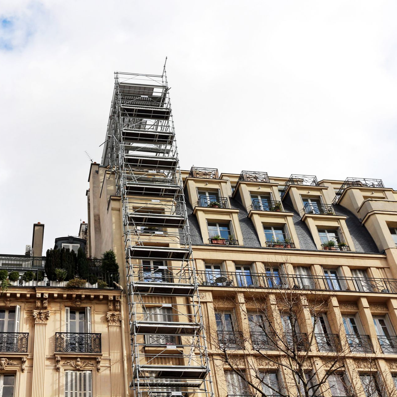Grand échafaudage sur un immeuble parisien à l'architecture ornée, sous un ciel nuageux.