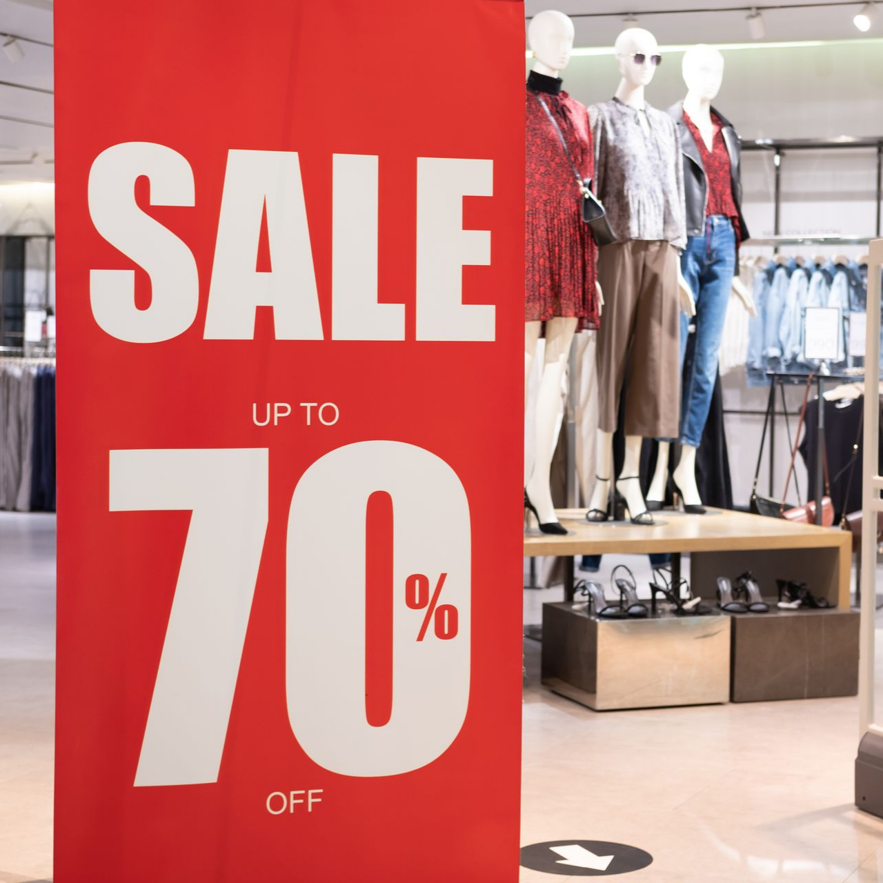 Panneau rouge SOLDES, jusqu'à 70 % de réduction, dans un magasin de vêtements avec mannequins et portants à vêtements.