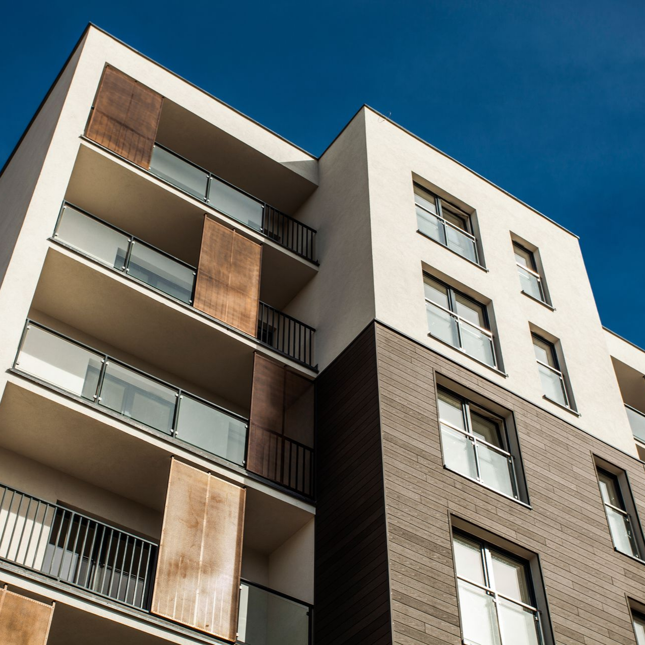 Immeuble d'appartements moderne avec façade blanche et brique, balcons et ciel bleu.