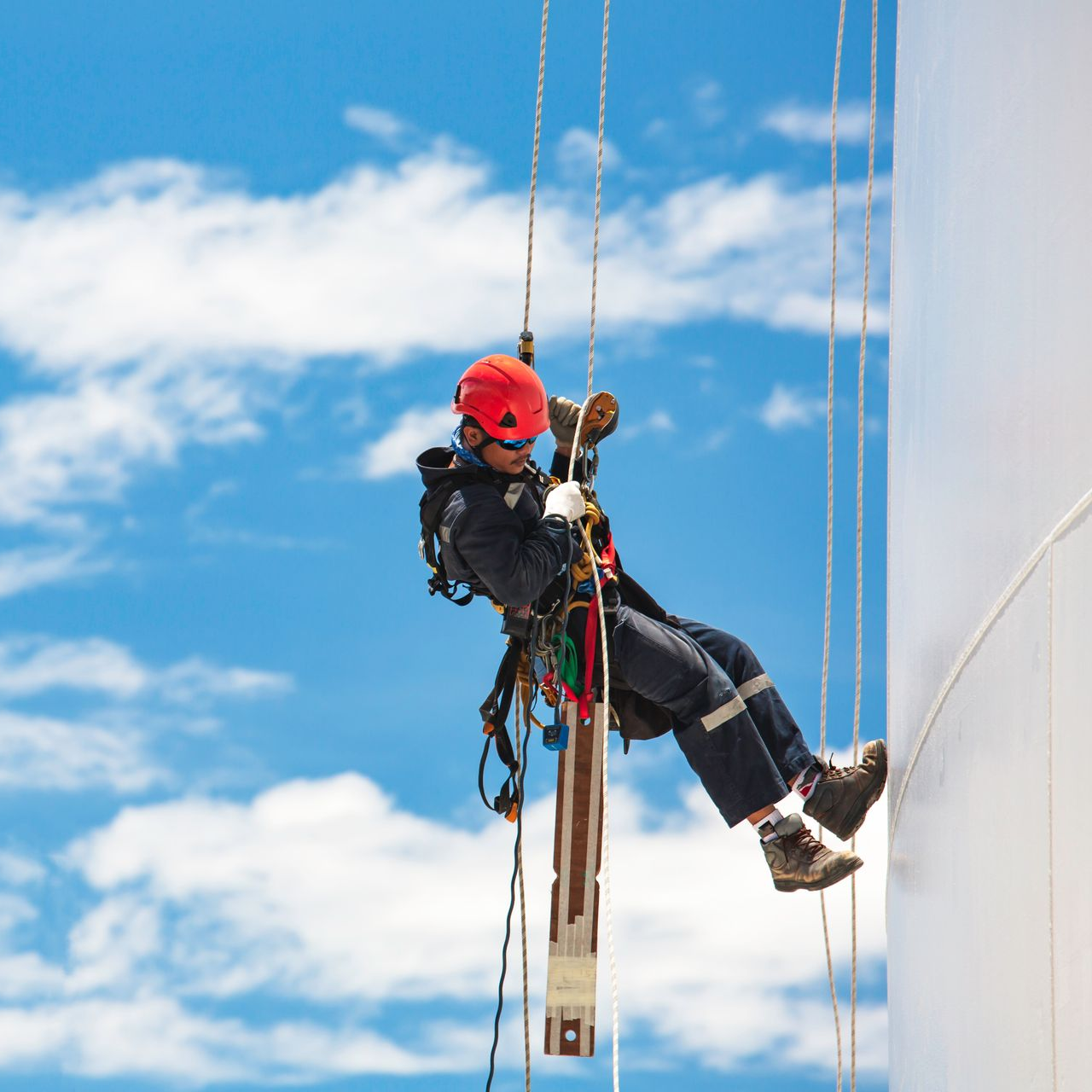 Une personne portant un équipement de sécurité descend en rappel le long d'une grande structure industrielle.