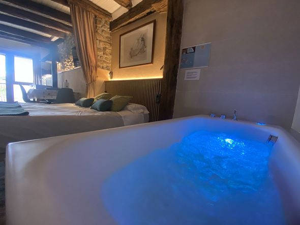 Bañera de hidromasaje con luces azules en un dormitorio, cerca de una cama y vigas de madera.