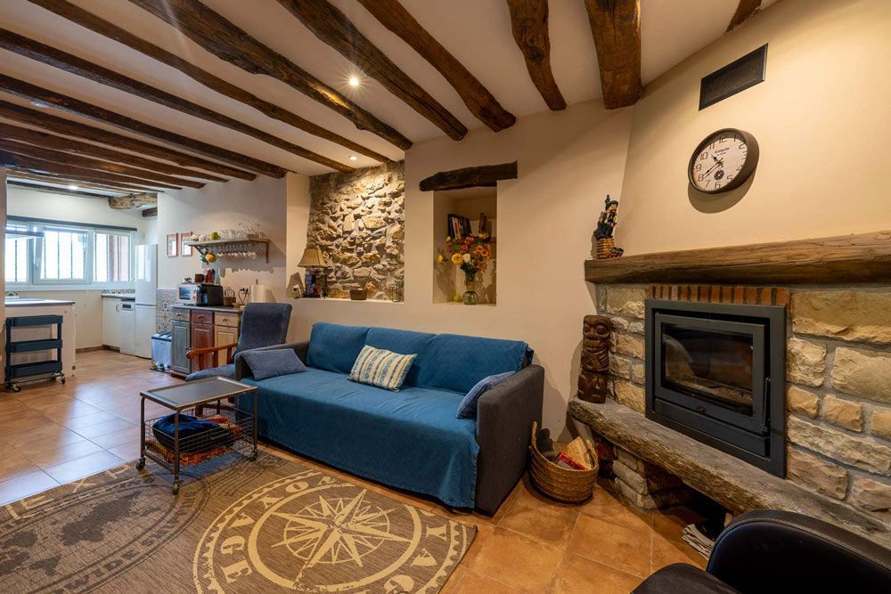 Acogedora sala de estar con chimenea de piedra, vigas de madera, sofá azul y alfombra redonda con diseño de brújula.