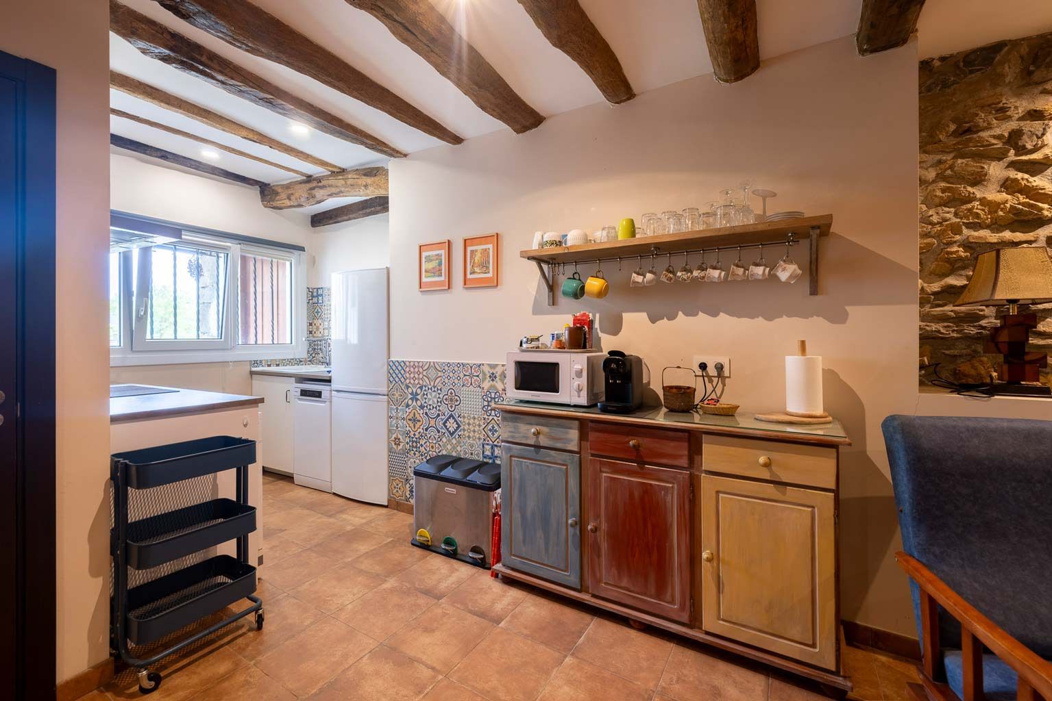 Cocina rústica con vigas de madera, gabinetes coloridos y pared de piedra a la vista.