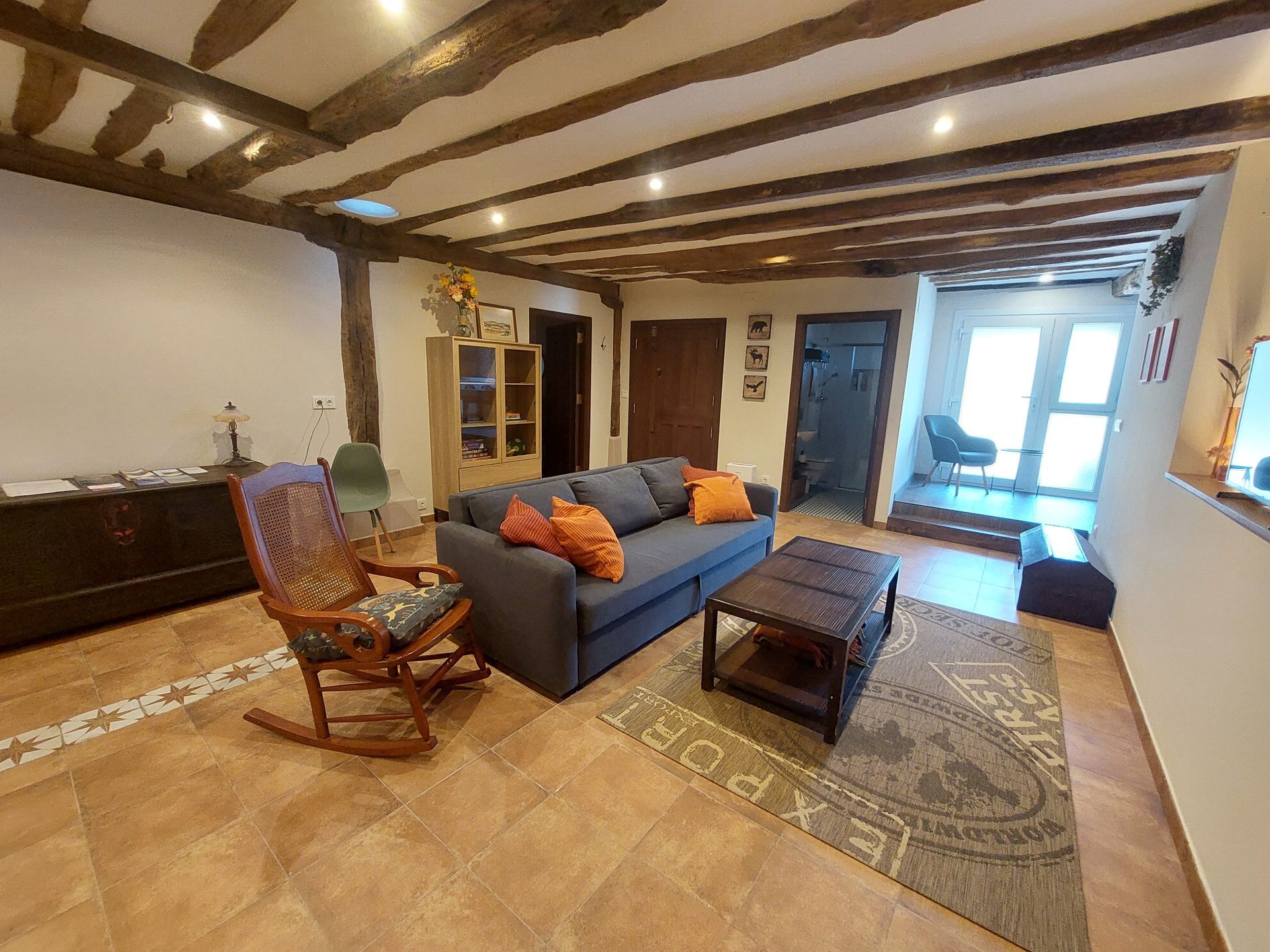 Dormitorio con cama de matrimonio, vigas de madera y puerta abierta a una pequeña cocina.