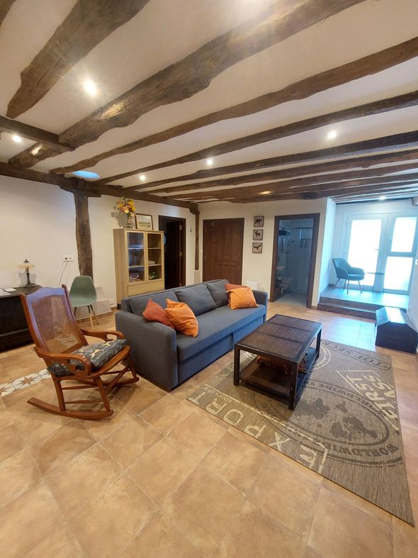 Dormitorio con cama, armario, vigas a la vista y puerta de acceso a la cocina.