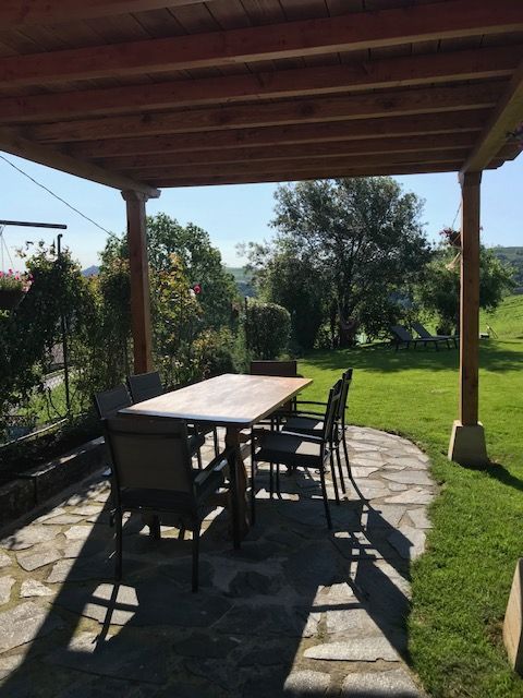 Comedor exterior bajo pérgola de madera, sobre patio de piedra, con vista al jardín.