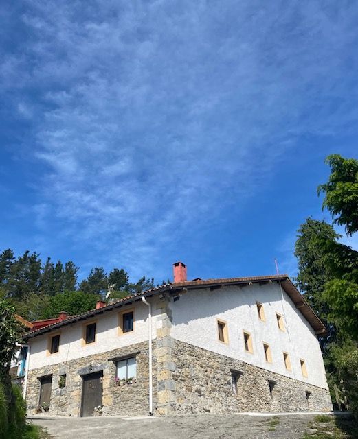 Edificio de piedra y blanco con techo de tejas rojas bajo un cielo azul con nubes tenues.