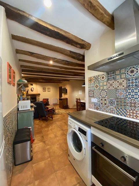 Cocina con salpicadero de azulejos, lavadora, estufa y vigas de madera rústicas en el techo, que conducen a la sala de estar.