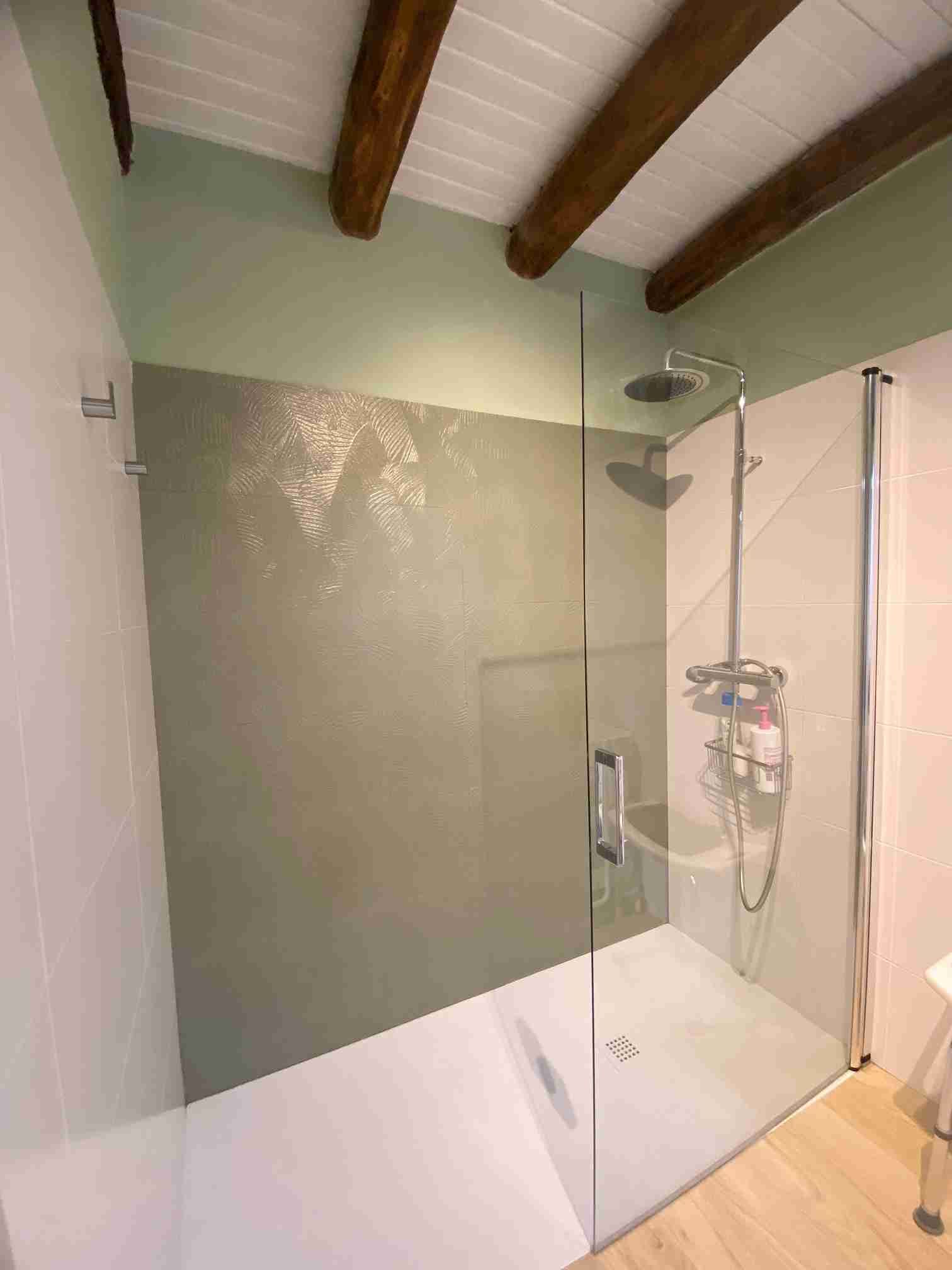 Ducha con puerta de vidrio, pared con acento verde, ducha superior y techo con vigas de madera.