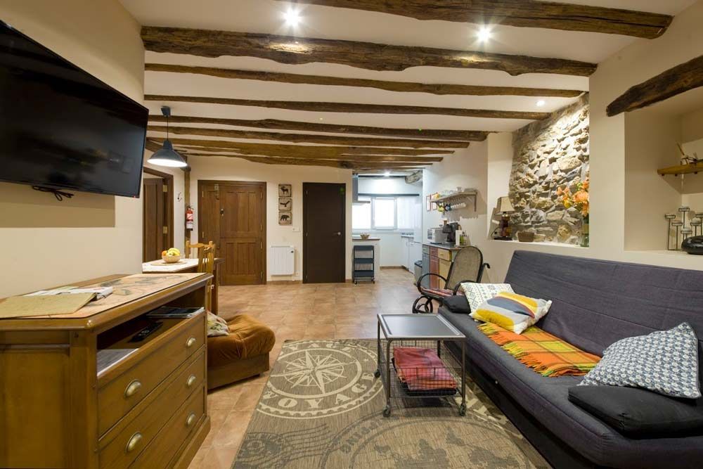 Sala de estar con vigas vistas, pared de piedra, sofá, TV y muebles de madera.