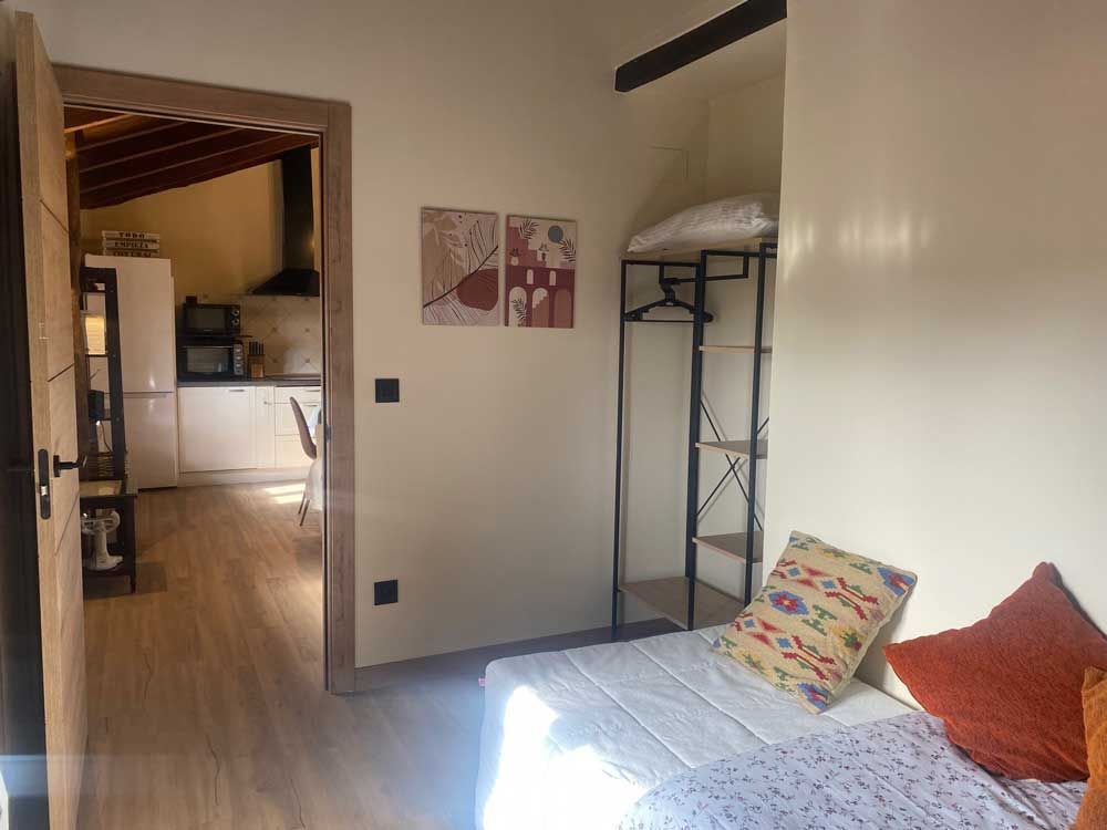 Interior con cama, puerta abierta a la cocina, arte en la pared y perchero.