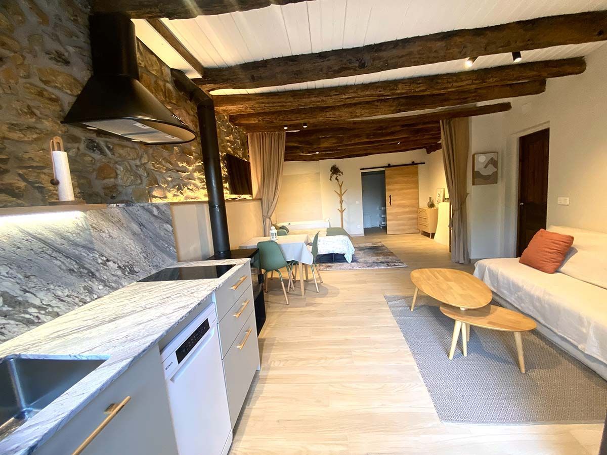 Apartamento moderno con cocina con paredes de piedra, comedor y sala de estar con vigas de madera.