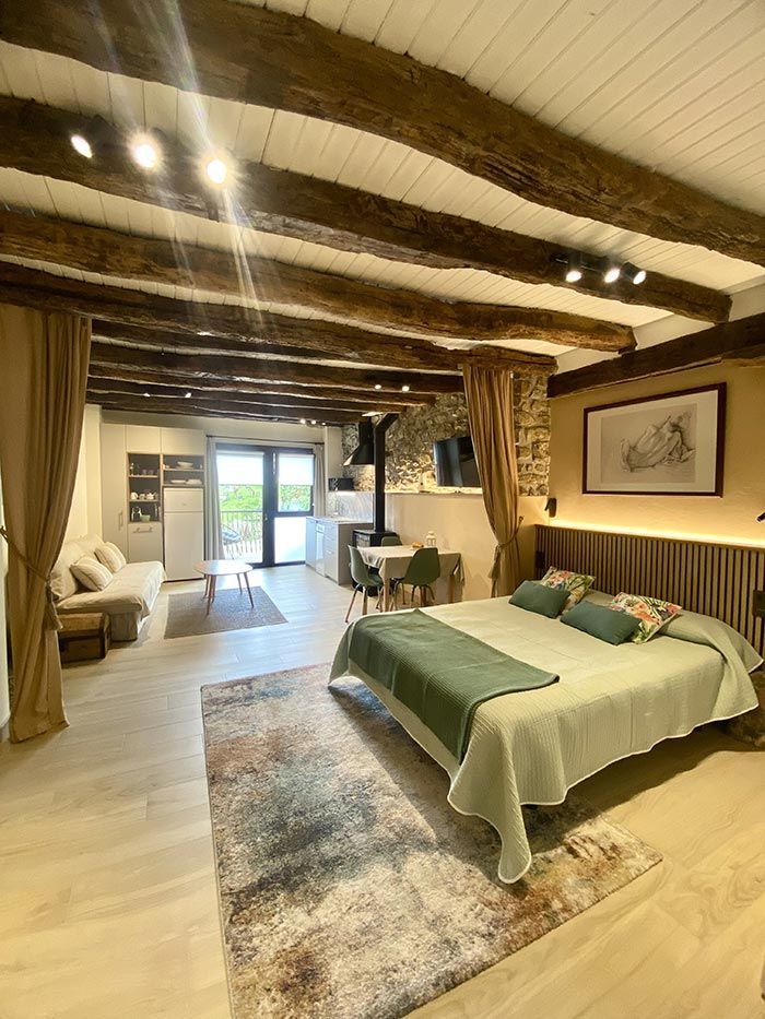 Acogedor estudio con vigas vistas, cama, sofá y cocina. Tonos cálidos e iluminación suave.
