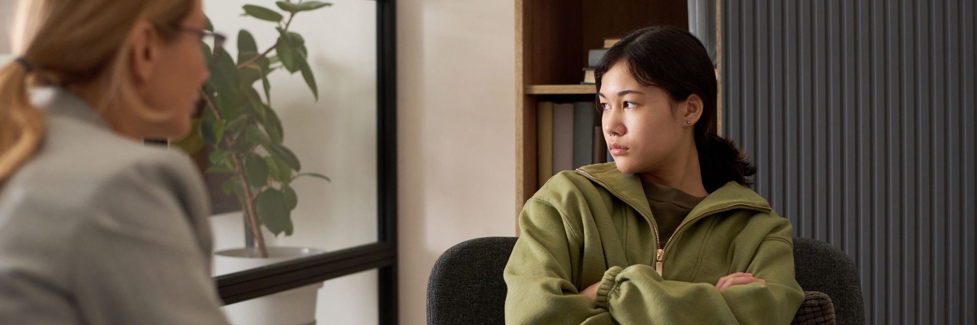 Femme en veste verte, assise les bras croisés, face à une femme qui parle hors champ. Intérieur.