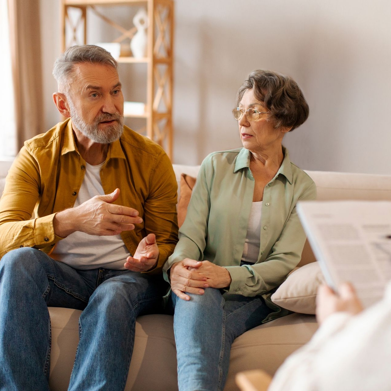 Un couple âgé, assis sur un canapé, discute avec une personne tenant un bloc-notes. Ils sont en séance de thérapie.