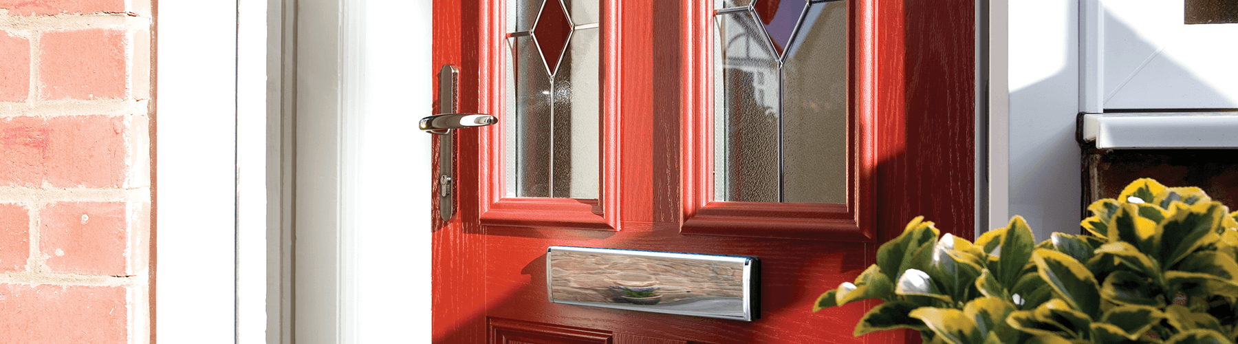 A red door with a stained glass window is on a brick building.