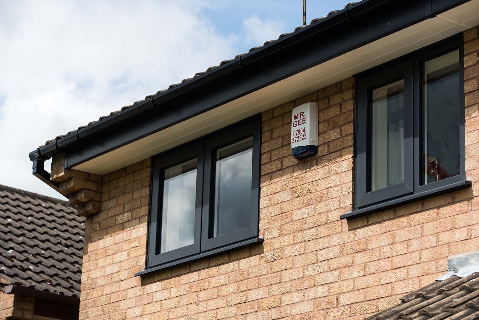 A brick house with black windows and a fire alarm on the roof.