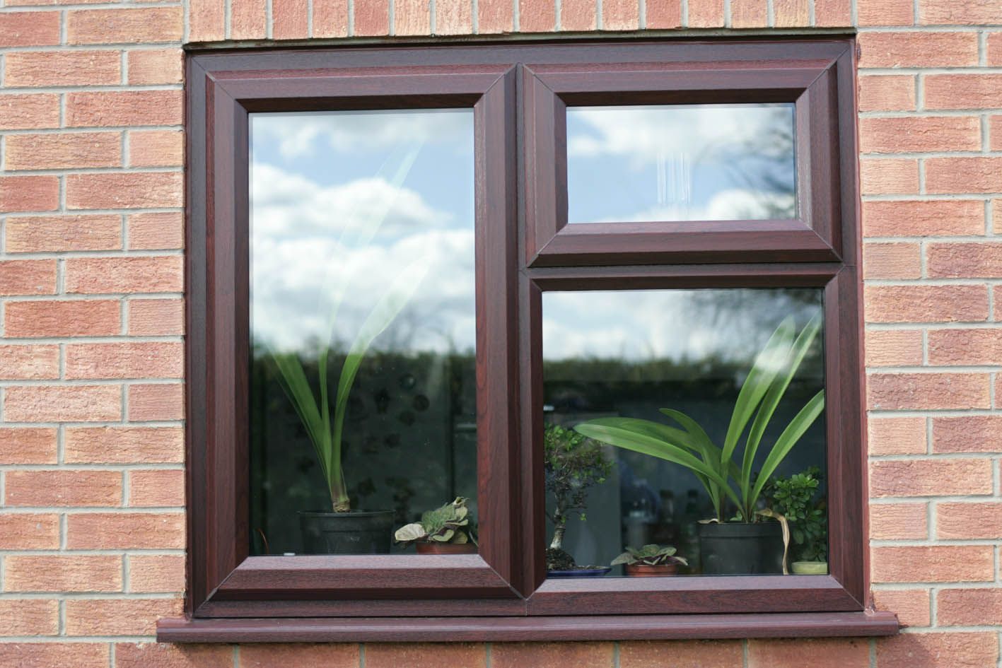 A window on a brick wall with two potted plants in front of it.