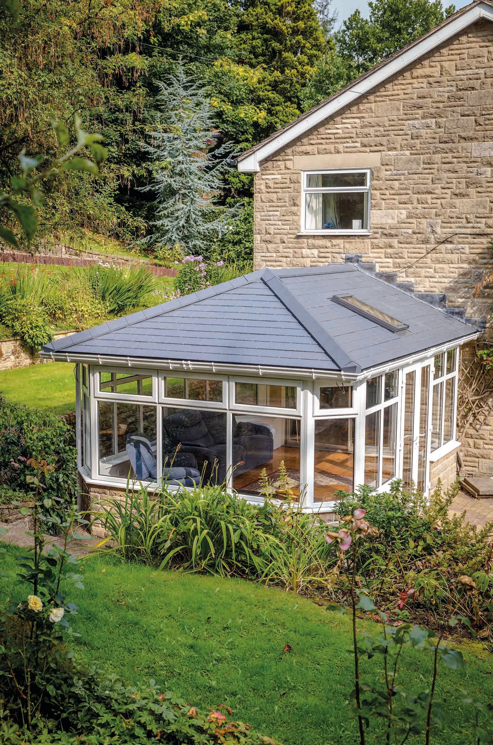 A conservatory with a slate roof is in the backyard of a house.