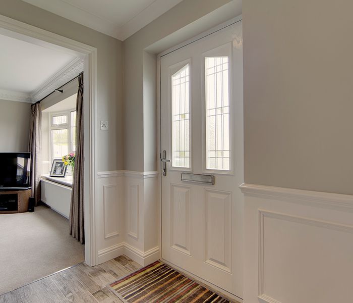 A hallway with a white door and a rug in it leading to a living room.