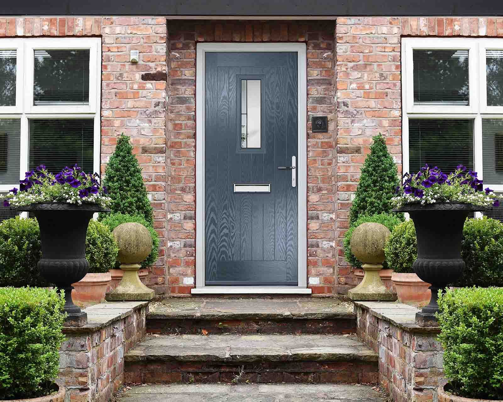 The front door of a brick house with a gray door and steps leading up to it.