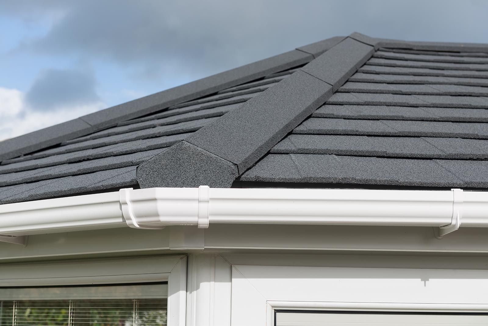 A close up of a roof with a white gutter and a window.