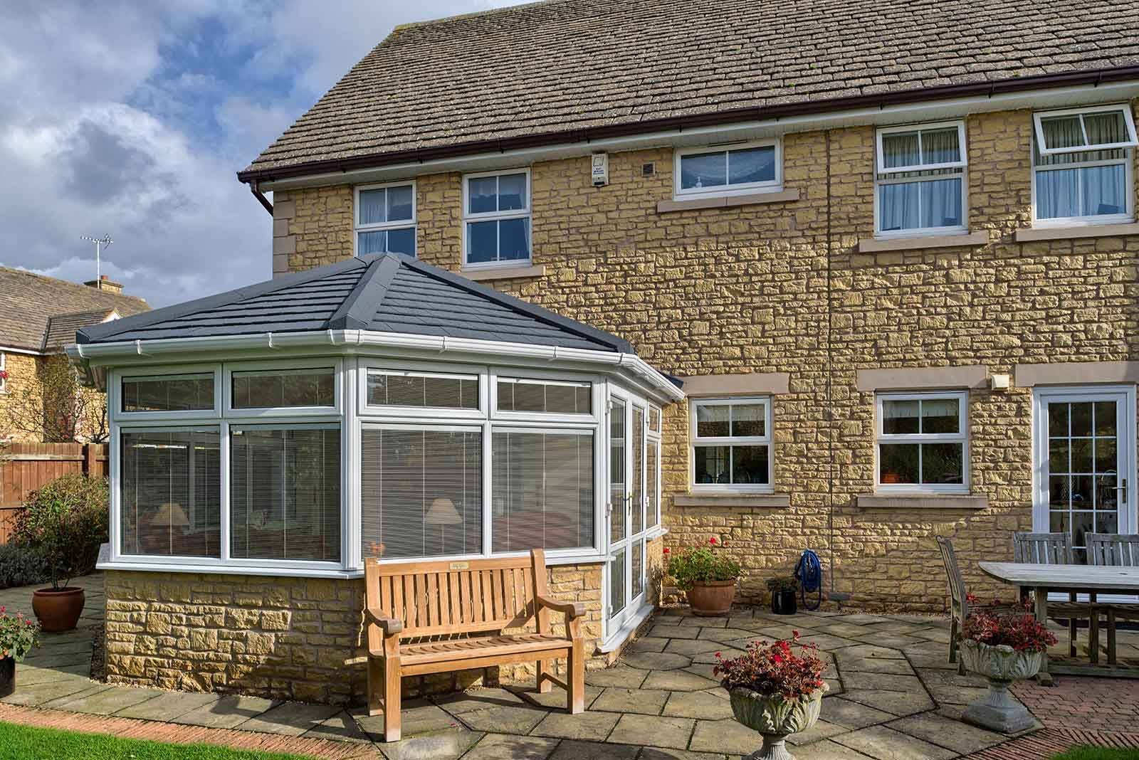 A house with a conservatory and a bench in front of it.