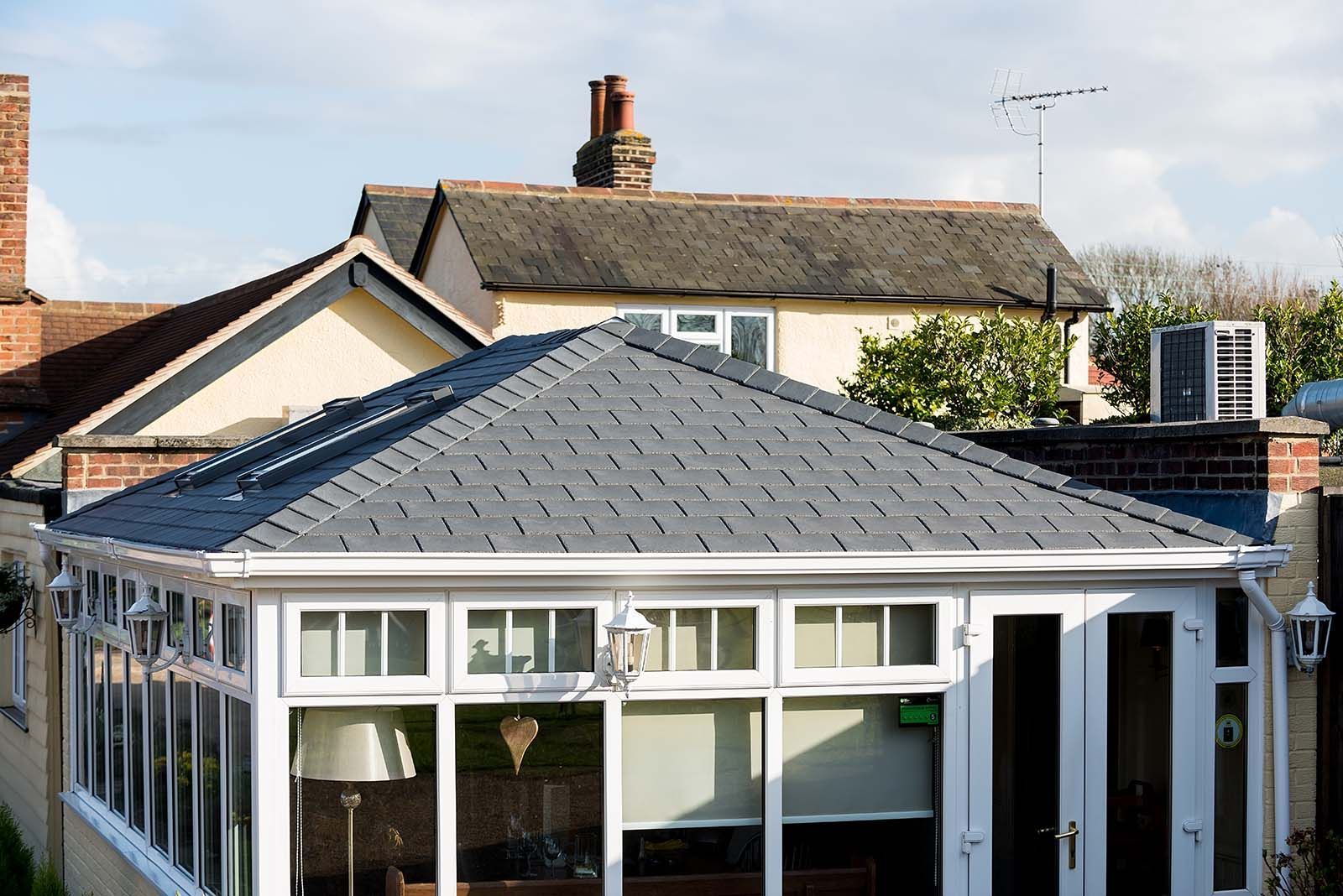 A conservatory with a slate roof is in the backyard of a house.