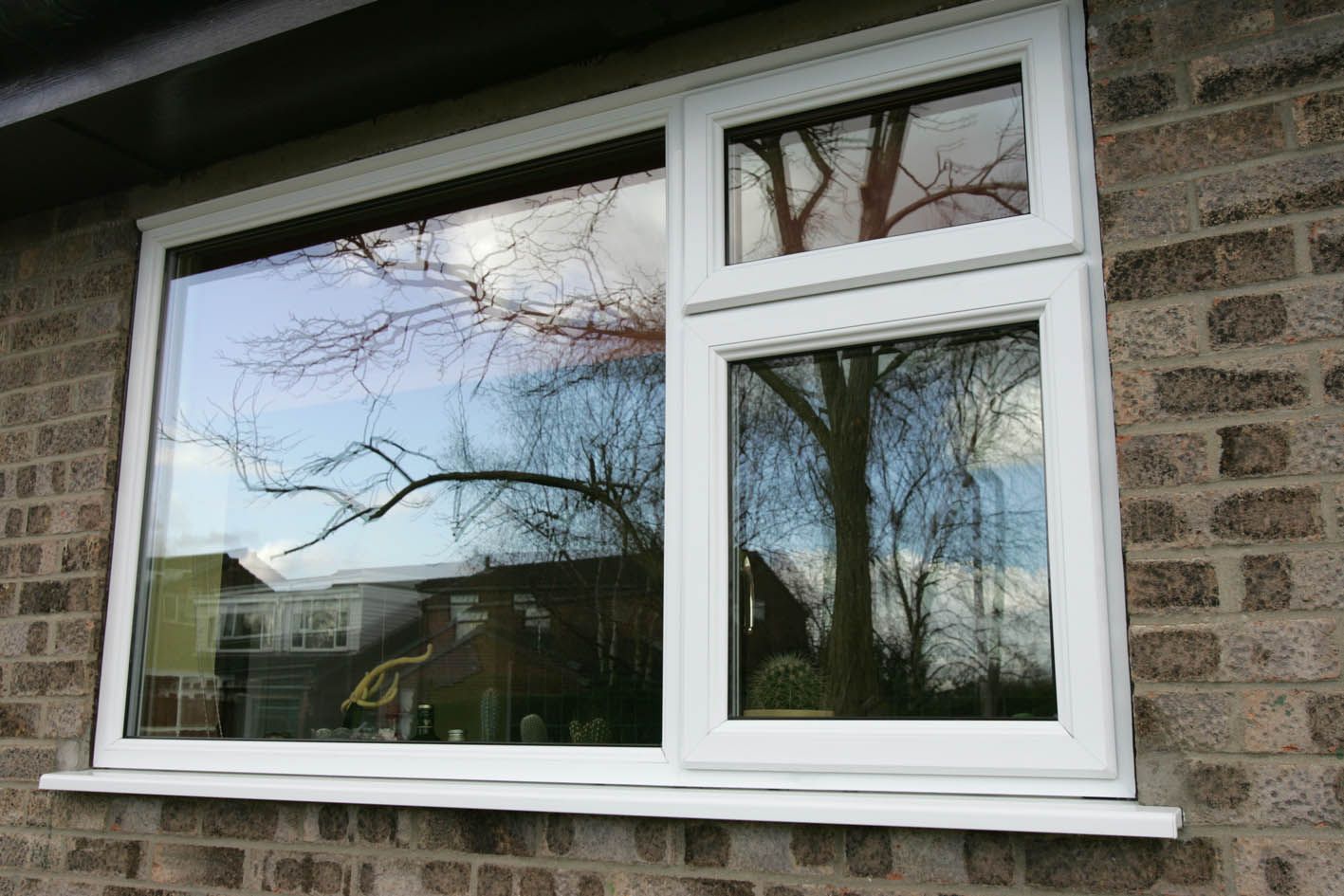 A white window is on a brick wall with trees reflected in the window.