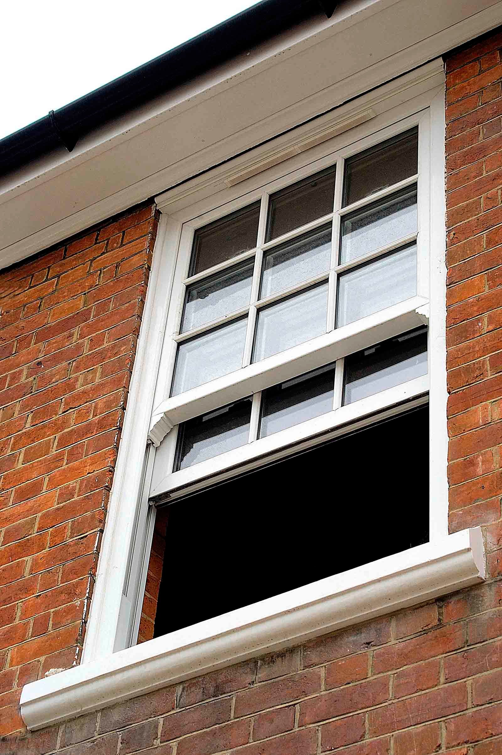 A white window is on the side of a brick building.