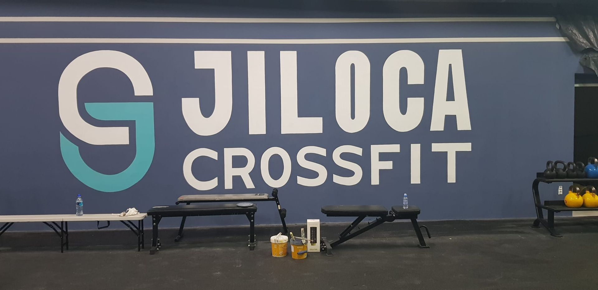 Persona alisando paneles de yeso con una llana grande de metal, con un guante rojo, en una esquina.